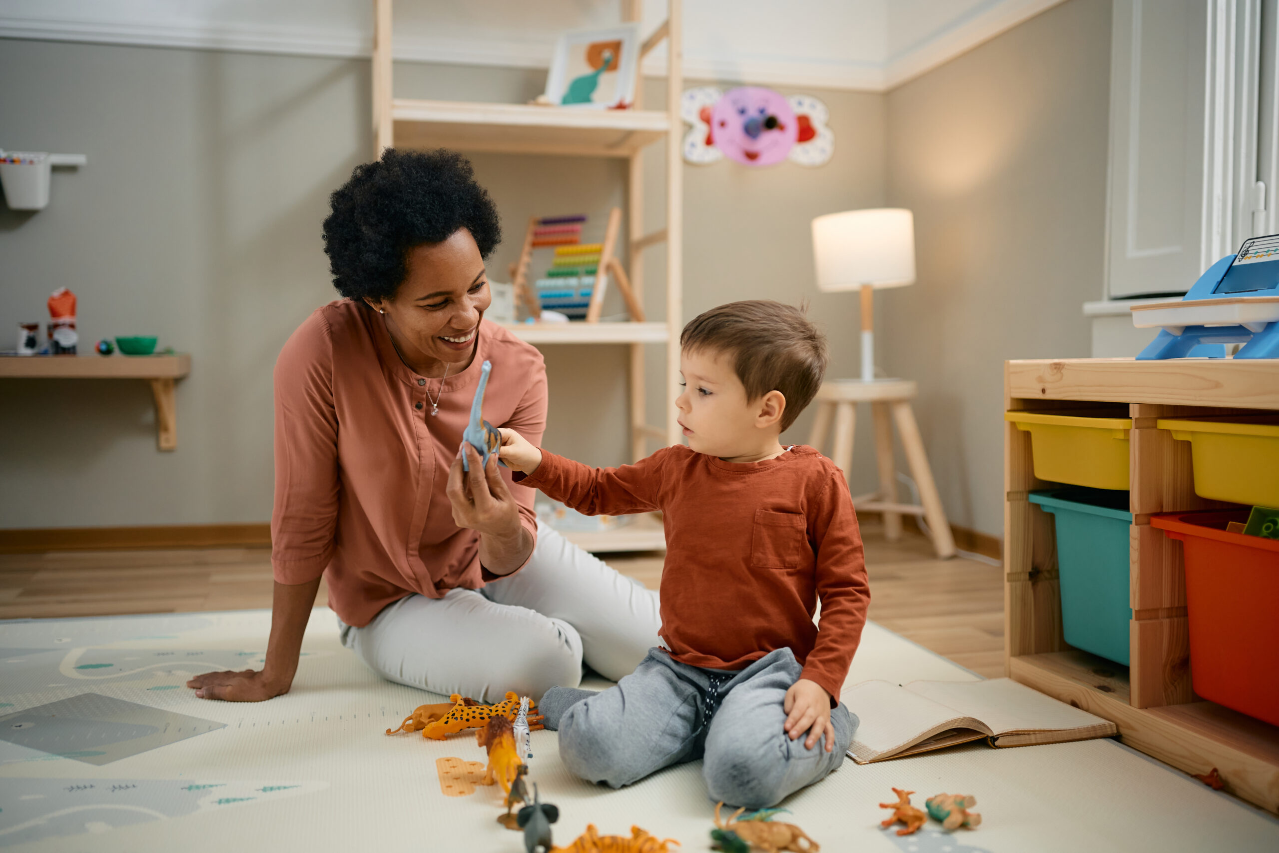 Happy black nanny and small boy playing with animal toys on the floor.